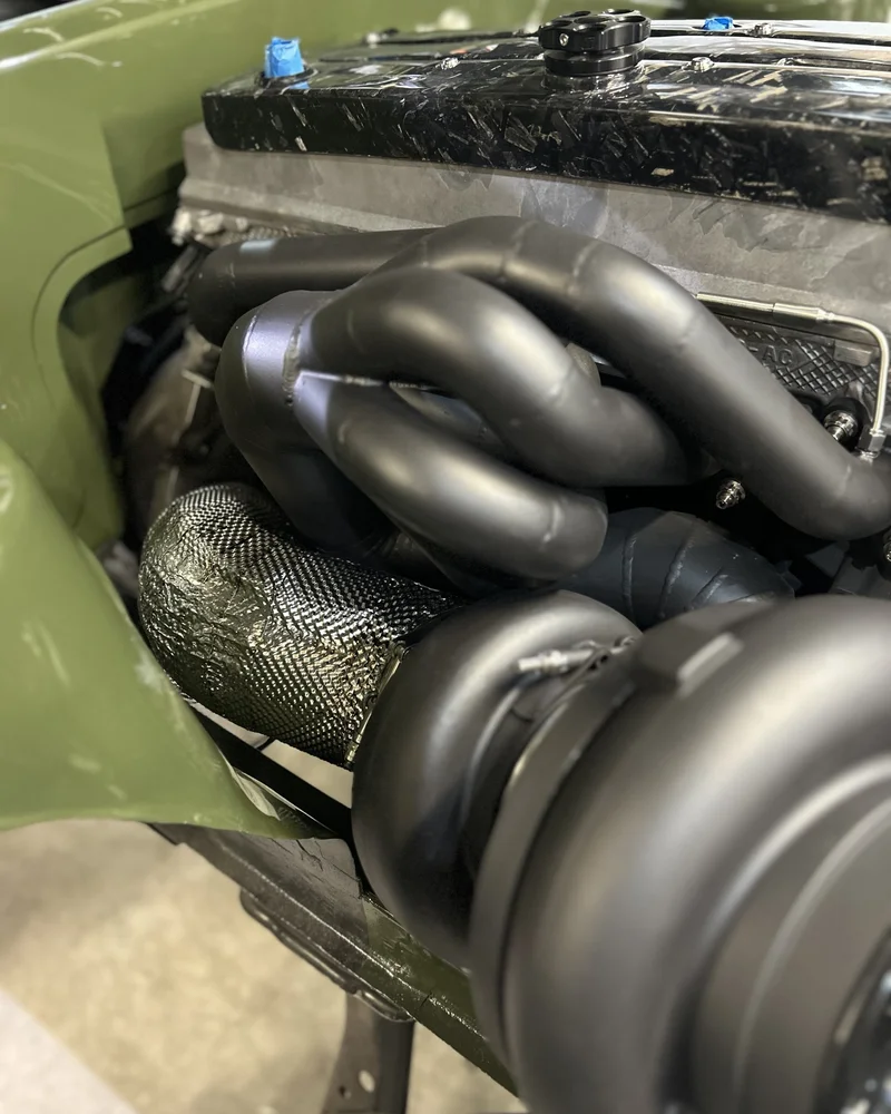 Integrated exhaust thermal shielding and turbocharger setup in a high-performance motorsport engine bay.