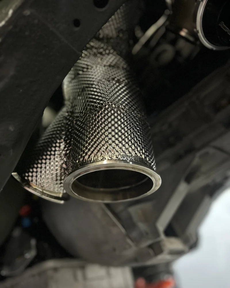 Close-up detail of a custom heat shield crimped and spot-welded to a V-band flange for an exhaust downpipe.