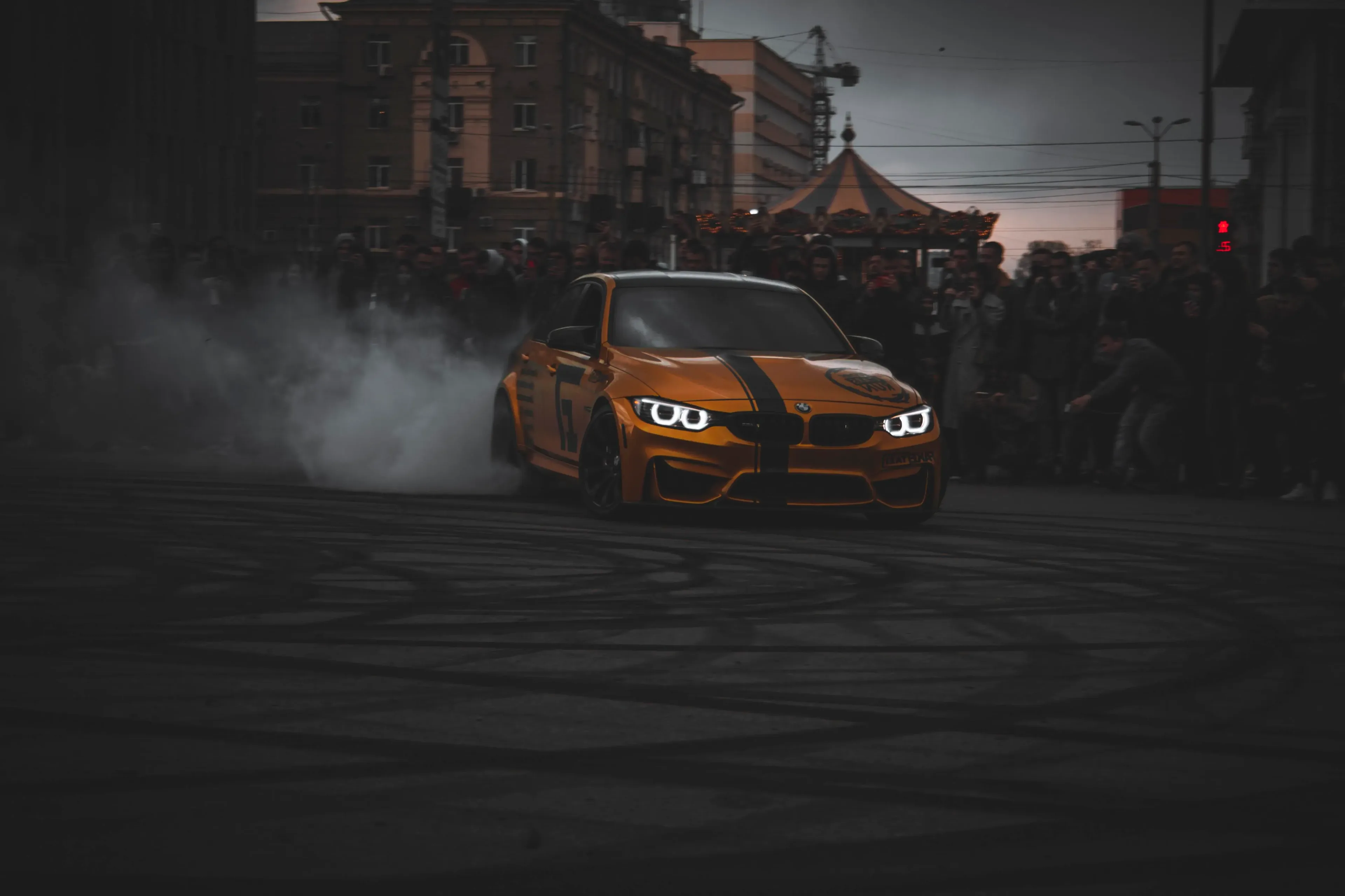 Orange BMW drift car performing a high-smoke burnout on a city street at a Bower Motorsport event